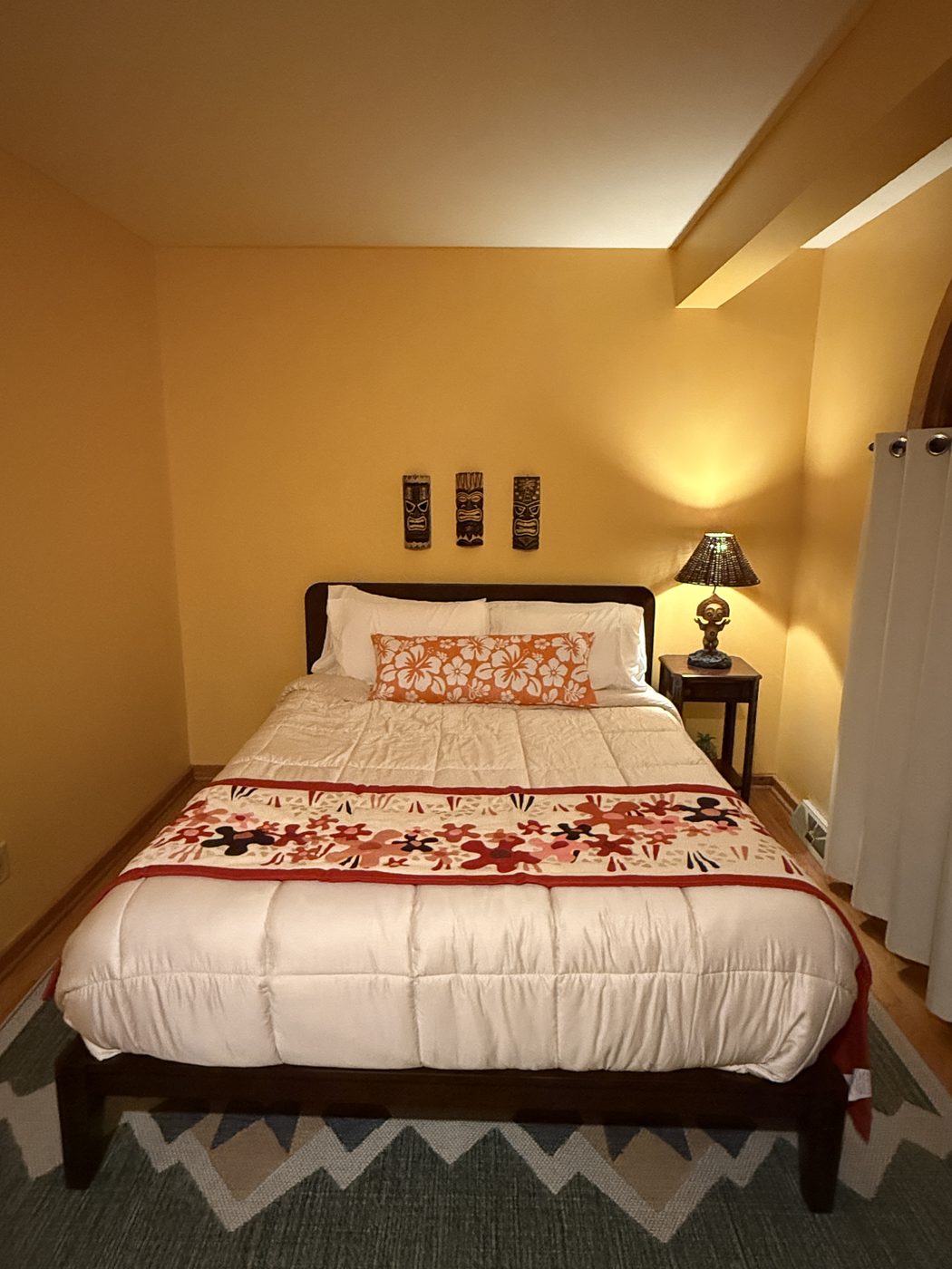 The guest room: bed with Hawaiian floral quilt, tiki masks on the wall, and a tiki lamp