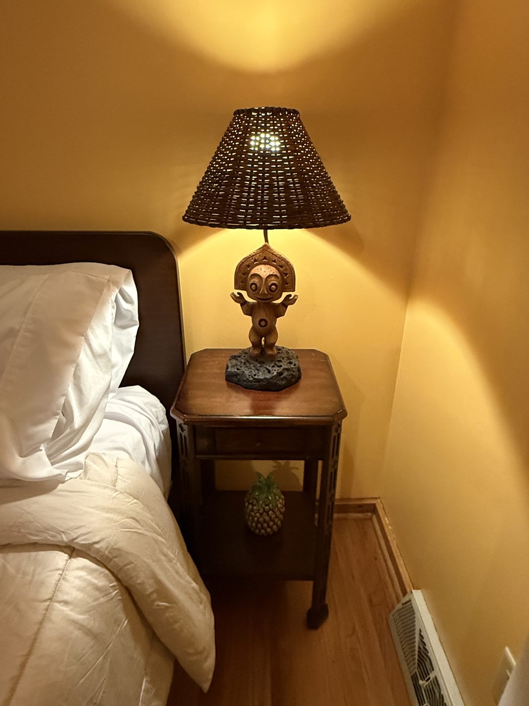 A carved tiki figure lamp with a woven shade glowing warm orange on the nightstand